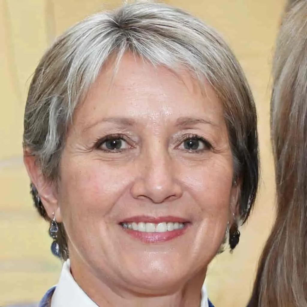 Two women stand close together, one with short gray hair wearing earrings, and the other with long brown hair, both smiling warmly.